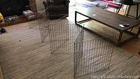 Full view of large metal dog crate panels set up in a living room, showing the connected wire frames and hooks for assembly.