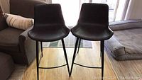 Front view of two black leather bar stools with metal legs positioned side by side.