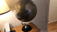 Front view of the decorative metallic globe on curved arm and black base, showing geographic details.