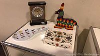 View of clock, llama figurine, spoon rest, and two inlaid marble coasters on table.