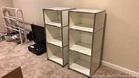 Two white metal shelf units with chrome frames, each unit featuring three open shelves, positioned in a carpeted room next to other furniture items