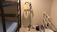 Full view of the metal floor lamp standing 56 inches tall with ornate scrollwork and cream lampshade, next to bunk bed and white metal bed frame.