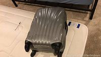 Front view of silver Samsonite carry on hard shell suitcase on a mattress.