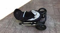 Folded black and beige Brutes B-Ready stroller positioned on ground showing compact fold and front locking wheels.