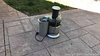 Side view of Breville Juice Fountain Juicer showing pulp container and attached power cord on patio floor.