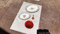 Photo of both porcelain trays and two orange glass pieces arranged on a white sheet outdoors.