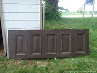 Old church door side with six raised panels leaning against building exterior on grass.