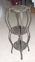 Full view of the black wrought iron plant stand showing three shelves with dragonfly patterns and curved supports.