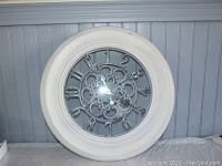 Photo showing the 23 inch round wall clock with light grey plastic frame and decorative mirrored clock face with black hands.