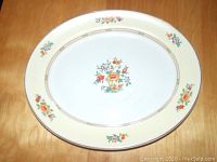 Full view of vintage oval Ambassador Ware platter with yellow border and floral designs on wooden surface.