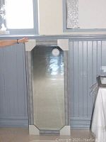 Full view of the tall rectangular mirror with shiny silver pebble effect frame, showing protective corner covers and reflection of background.