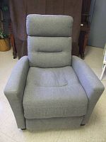 Recliner chair in upright sitting position, showing wide padded armrests, cushioned backrest, and grey fabric upholstery.