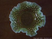 Top-down view of vintage yellow Vaseline Fenton hobnail opalescent milk glass dish with ruffled edges on a dark wooden surface.