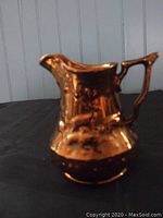 Photo of copper lusterware cream pitcher with deer relief design, showing the front and side profile including handle and spout.