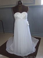 Front full length view of a white strapless bridal gown on a mannequin showing beaded bodice and flowy skirt with train.