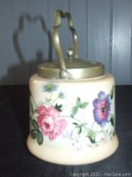Front angle of the vintage porcelain biscuit jar showing floral patterns and brass lid with handle