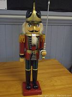 Front view of the 25-inch tall wooden nutcracker soldier figurine in uniform standing on a red base.