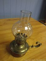 Side view of the brass finger lamp showing the bulb holder and clear glass globe on wooden surface.