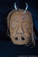 Full front view of mask showing horns, carved faces, mouth detail and hair fringe