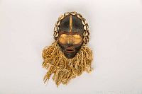 Front view of full mask showing carved face, cowrie shell border and fiber fringe