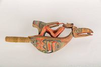 Side view of rattle showing stylized bird head and painted formline designs.