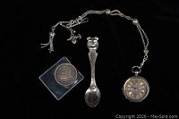 Overview of all three items: silver spoon, Canadian silver dollar coin, and silver pocket watch with chain on black background.