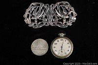 Silver belt buckle, 1939 Canadian silver dollar, and ADY pocket watch displayed on black cloth.