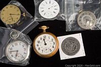 Group photo of three pocket watch movements, one complete British Army pocket watch, and an 1886 US silver dollar coin