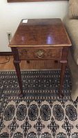 Wood end table viewed from top, showing the drawer front, brass pull handle, and wood grain.
