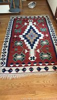 Full view of rug on hardwood floor showing overall geometric design and fringe