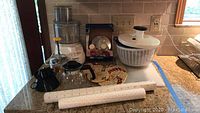 Front view of Cuisinart food processor with attachment and accessories including colander, salad spinner, and trivets.