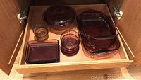 Amber Pyrex baking dishes of various sizes stacked inside a wood cabinet drawer.