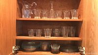 Wide shelf view showing clear glass pitcher, several drinking glasses, plates, and bowls