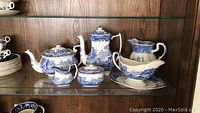 Full set of blue and white Spode serving pieces displayed on glass shelving including coffee server, teapot, water pitcher, gravy boat, sugar and creamer.