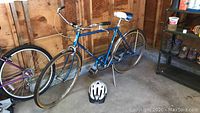 Full view of men's vintage Schwinn Collegiate bike in blue with helmet placed in front on the floor, showing overall condition and surroundings.