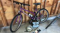 Full side view of purple Diamond Back Sorrento bike with helmet and accessories on floor nearby