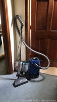Full view of assembled Miele Plus S2511 canister vacuum with hose and wand standing upright on carpeted floor.