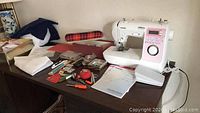 Overall view of sewing machine, foot pedal, manual, and assorted sewing supplies arranged on table