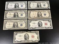 Seven vintage U.S. currency bills showing $1 silver certificates and $2 red seal notes laid flat on a black surface.