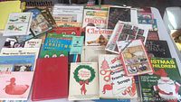 Photo showing many vintage craft instruction books and booklets with Christmas and holiday-themed covers, colorful and illustrated.