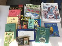 Photo shows a variety of nature and teaching books and magazines arranged on a table, titles visible include guides to insects, birds, ecosystems, and publications like Ranger Rick's NatureScope.