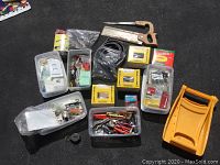 Overall view of plastic bins and tools grouped together on black carpet showing saw, snow shovel, screwdriver, and various boxes of nails and fasteners.