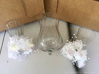 Three glass candelabra tops, two smaller decorated with white flowers and faux pearls, one larger plain glass piece in center.