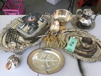 Overview of all silverplate serving pieces grouped together showing trays, teapot, gravy boat, spoon, and other utensils.