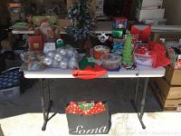Wide view of the lot on a white table showing the tree, ornaments, boxes, peg board with figurines, and gift bags.
