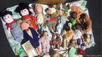 Full view of assorted vintage and antique dolls laid on cloth with basket background