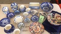 Full view of the blue and white china collection on table showing multiple plates, bowls, cups, a vase, and a rectangular planter with blue patterns.