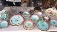 Wide view of grouped antique and vintage glassware and porcelain items including Adams Calyxware tea cups, plates, clear pressed glass bowls, oil lamp and glass cloche.