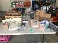 Overview of all wedding items arranged on a folding table including boxed favors, decorative signs, glass bottles, and votive holders.