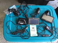 Lot of three GPS units including Garmin Street Pilot c330, Garmin Nuvi 52LM, and Magellan Maestro 4040 with various power cables and mounts on a blue container lid.